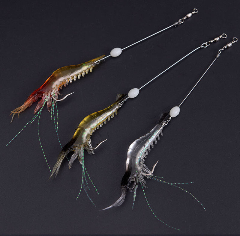 Three fishing lures shaped like shrimp or prawns, each attached to a long silver wire with a white bead and split ring, displayed on a dark background.