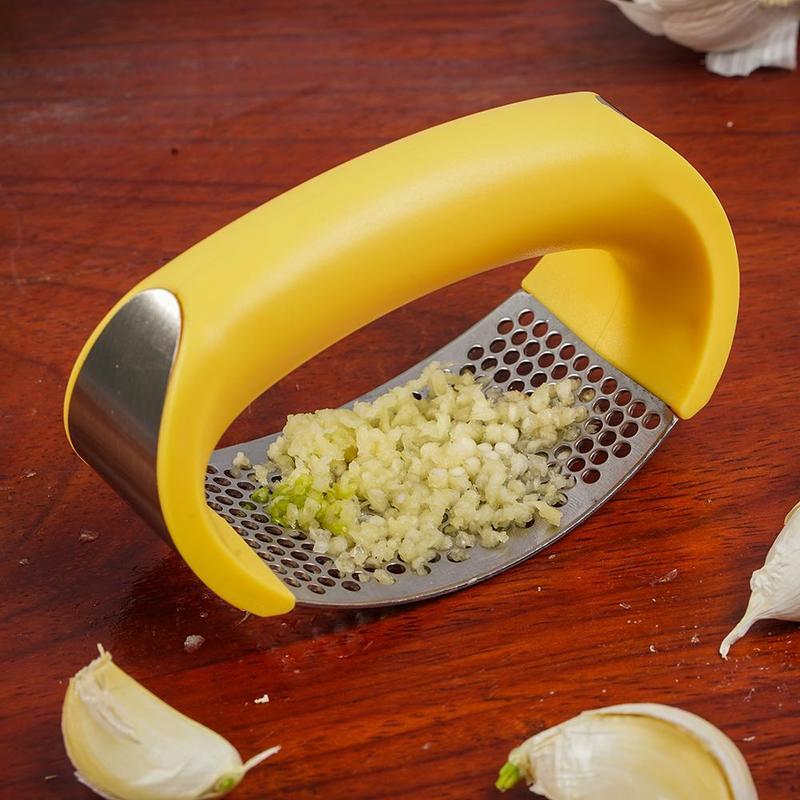 Yellow garlic press with minced garlic on a wooden surface