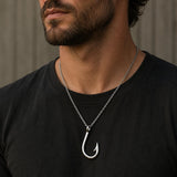 Man wearing a black shirt with a silver fish hook necklace.