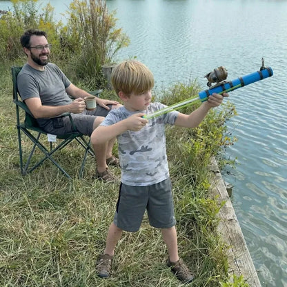 Man sitting in a chair by a lake, watching a child with a toy fishing rod.